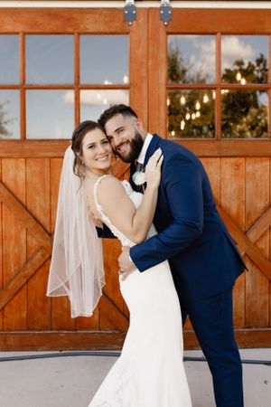 Newlyweds share intimate moments in front of rustic orange barn doors.