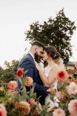 Romantic wedding couple sharing an intimate moment in a garden with pink and coral dahlias in bloom.