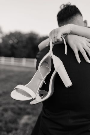 A black and white photo showing white bridal heels being held against formal attire.