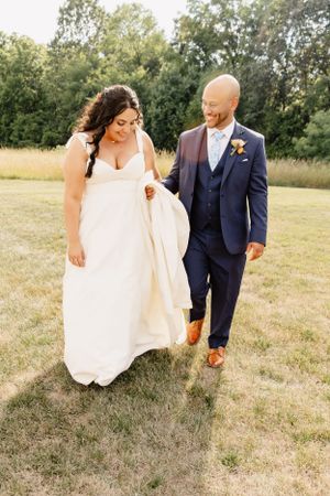 A couple walks hand in hand through a sunny meadow on their wedding day.