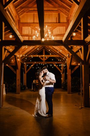 A romantic moment captured in a rustic wooden barn venue illuminated by warm string lights.