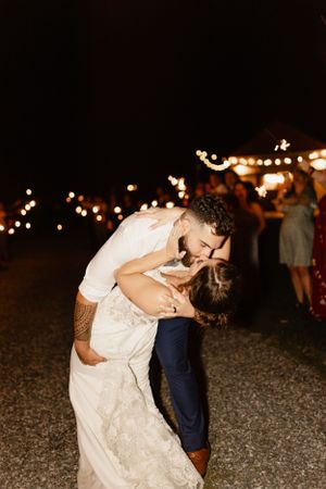 A romantic evening dance moment captured under twinkling lights at an outdoor reception.