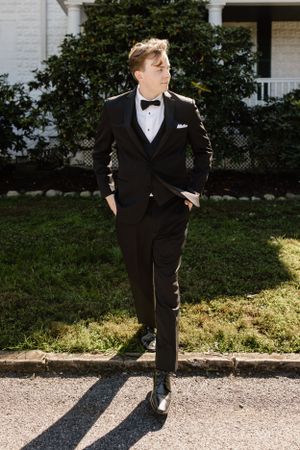 Young boy in formal tuxedo poses playfully in multiple shots outside white building.