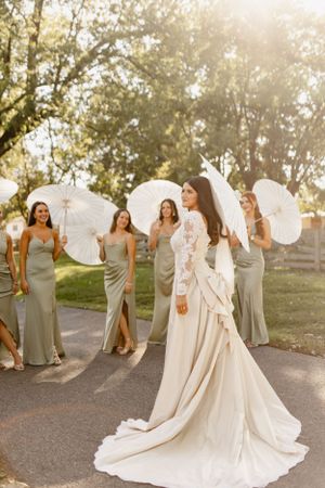 Wedding party in grey bridesmaid dresses gathering around bride in flowing white gown during sunset.