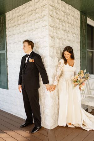 Wedding party poses against white stone wall in classic black and ivory attire.