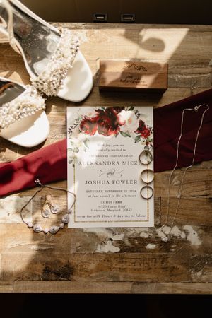 Rustic wedding invitation with floral design laid on wooden surface with accessories.