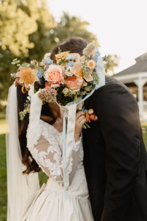 Elegant wedding couple with peach and blue floral arrangements against garden backdrop.
