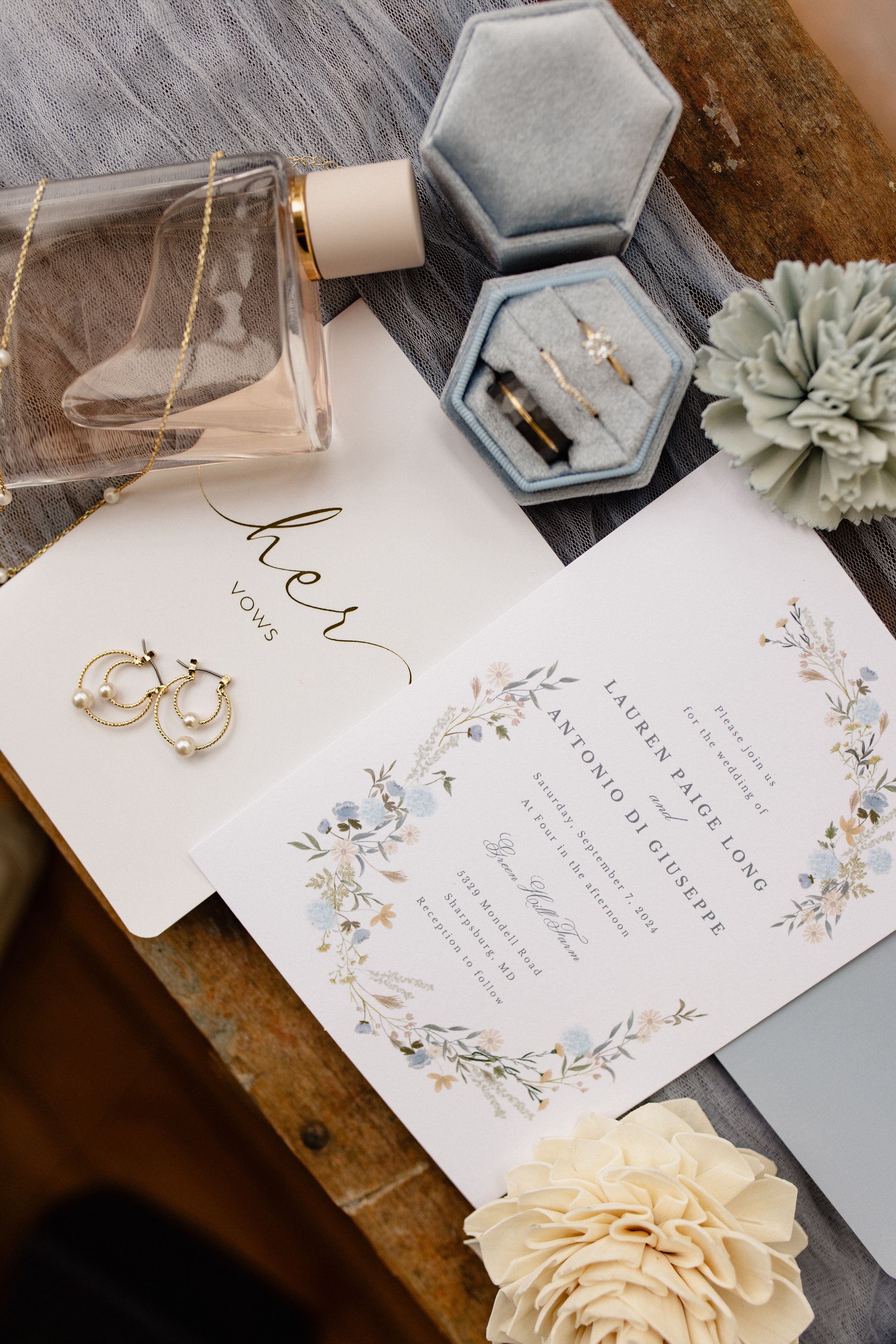 Wedding details flatlay with invitation, perfume, jewelry box and delicate floral design.