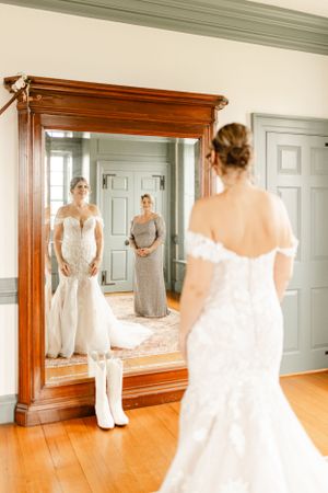 A full-length mirror reflects a wedding dress fitting in an elegant room with hardwood floors.
