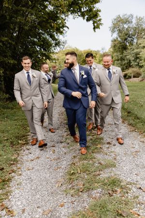 Groomsmen walking down a gravel path wearing coordinated suits in navy and gray.