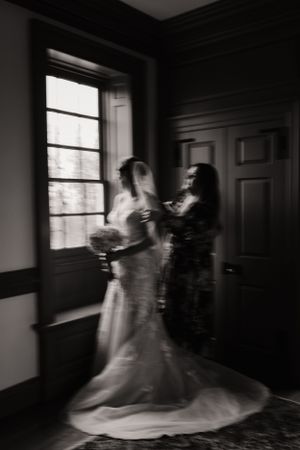A black and white artistic photo of a bride getting ready by a window.