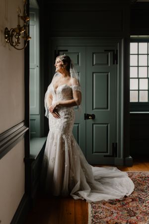 A lace wedding dress with long train captured in dramatic window lighting.
