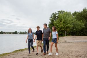 Group of people walking together along a sandy beach path next to a serene lake on an overcast day.