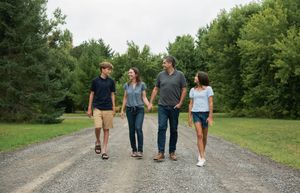 A group of people walking together on a gravel path through lush green woods on a summer day.