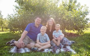 A family sits together on a blanket for a casual outdoor portrait in an orchard.