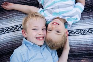 Two children laying on a striped blanket sharing a playful moment together.