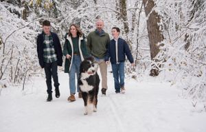 A family and their husky dog walk together on a snow-covered trail in winter.