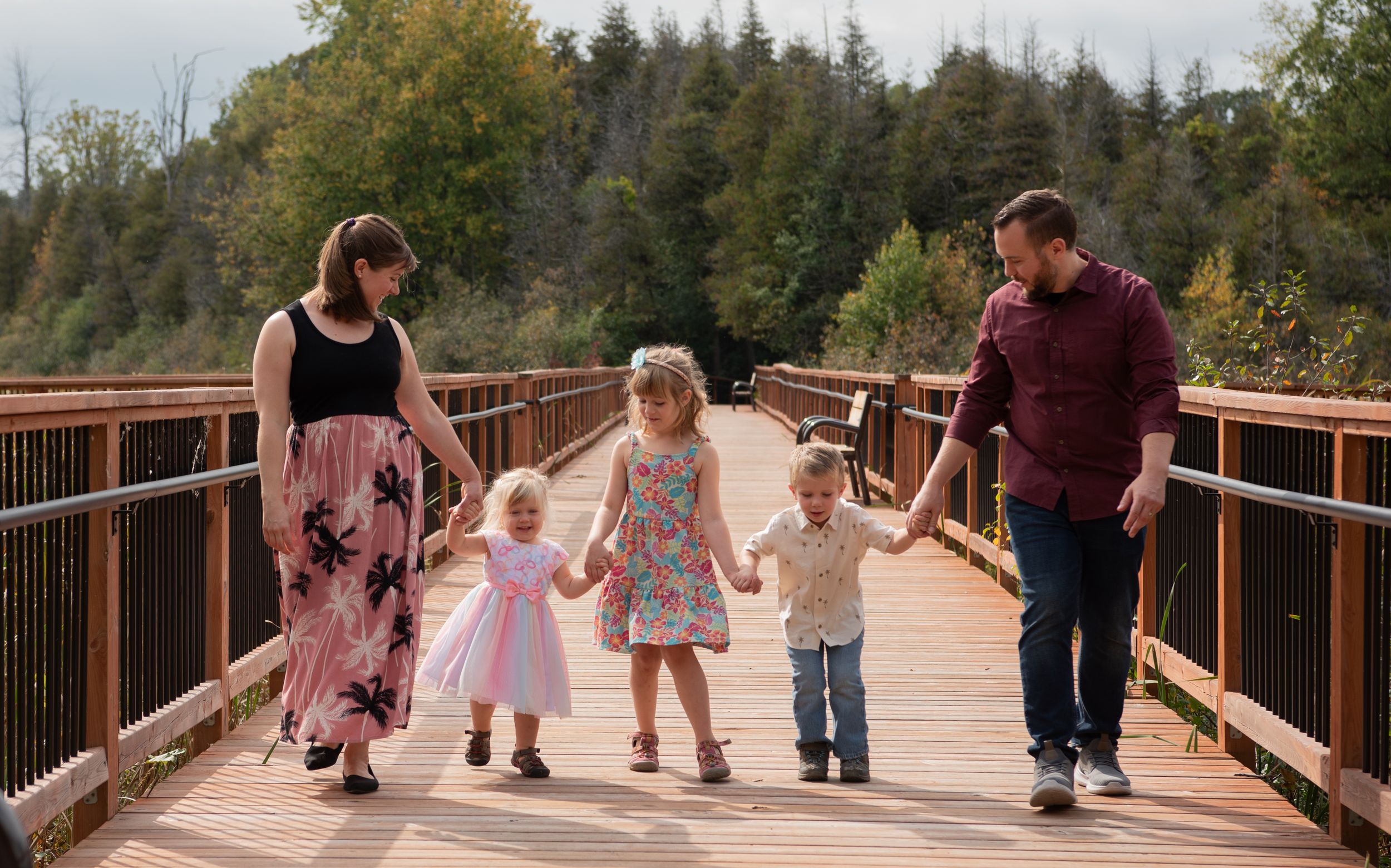 A panoramic view of people walking and enjoying a scenic wooden boardwalk through a forested area on an autumn day.