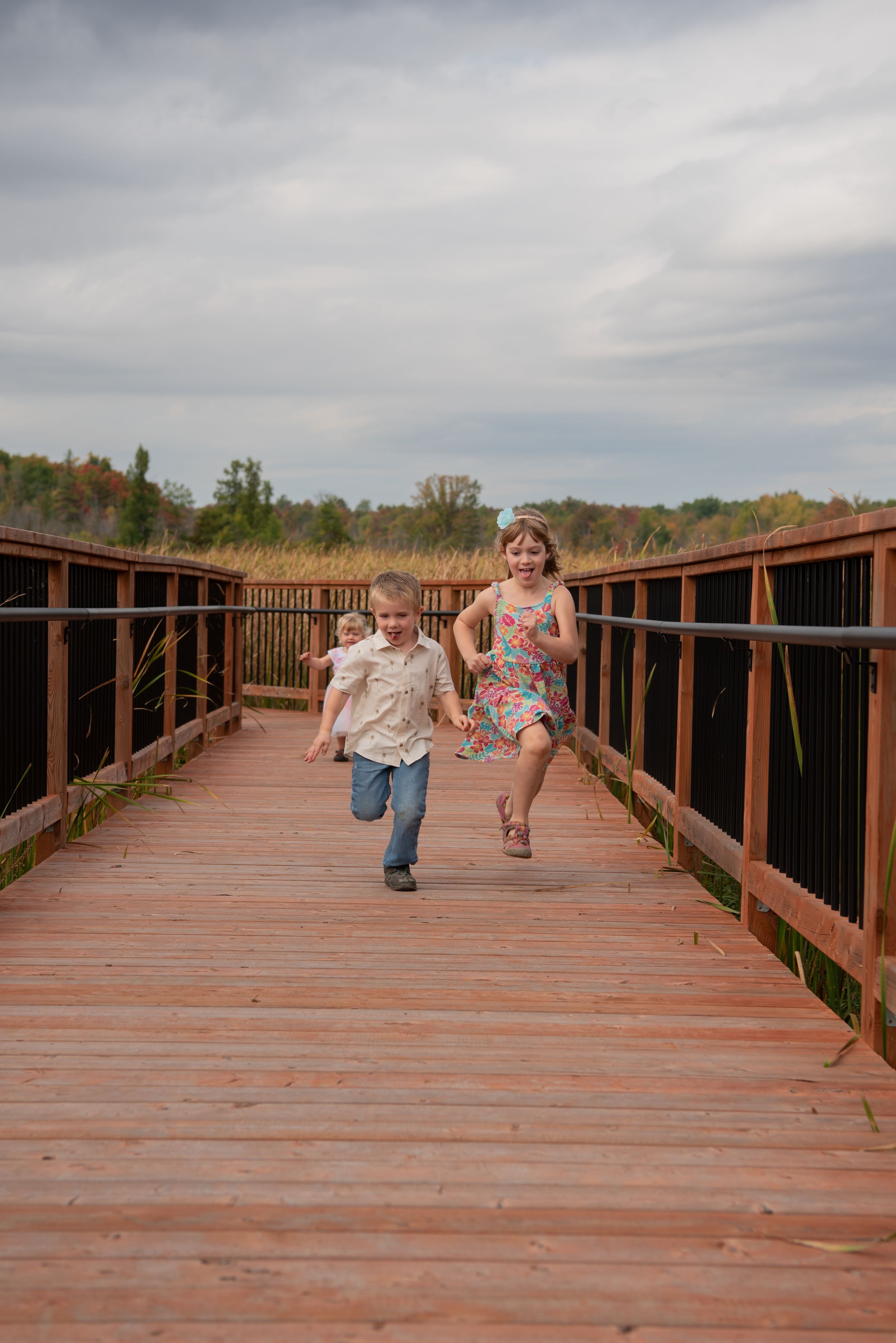 Children run and play on a long wooden boardwalk bridge on a cloudy day in a sequence of action photos.