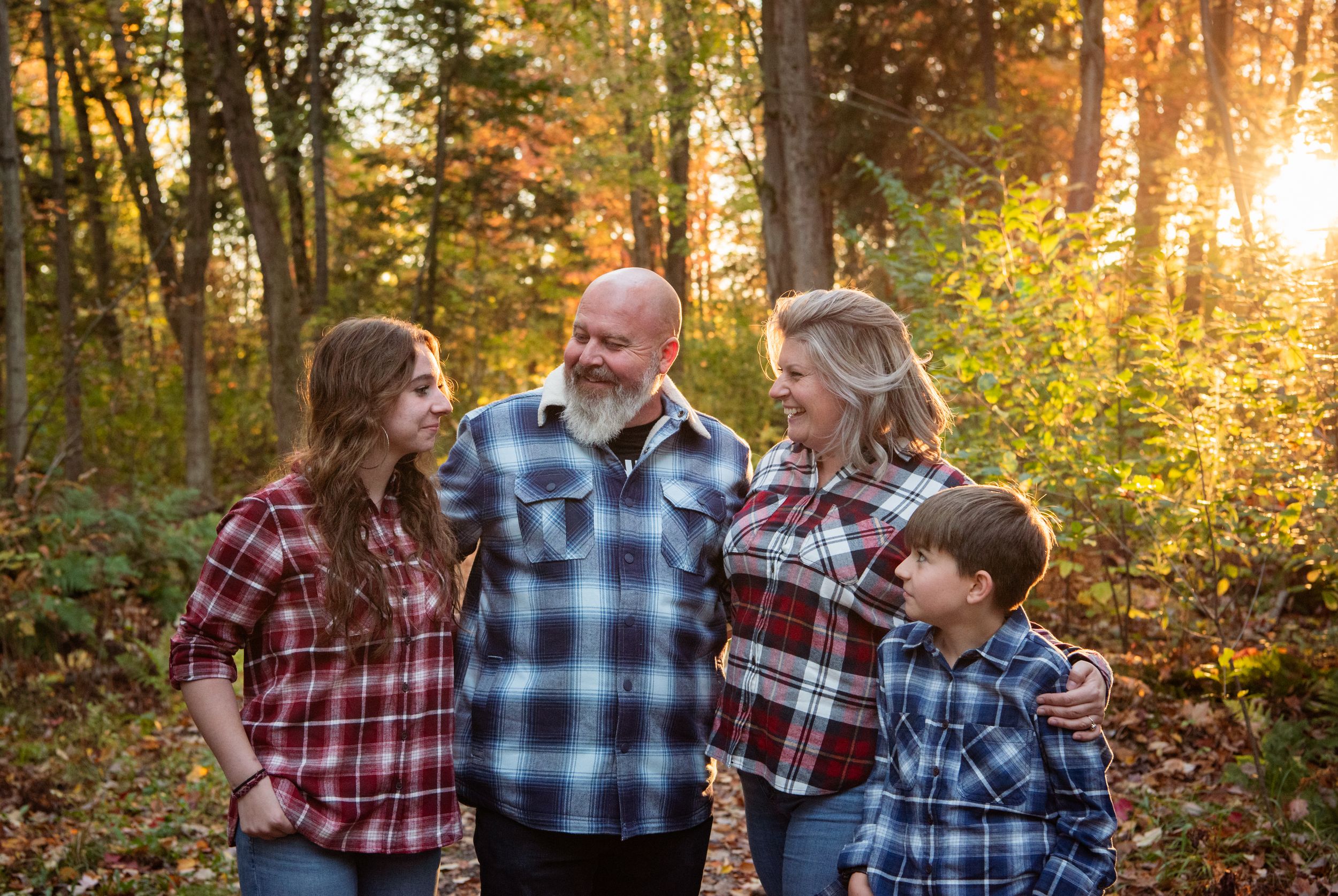 A family enjoys a golden autumn sunset together in the woods wearing coordinating plaid and denim outfits.