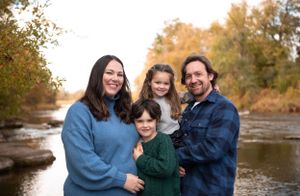 A loving family poses together by a rocky stream during autumn.