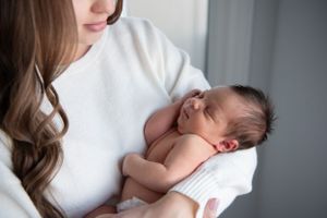 A newborn baby rests peacefully on a white sweater as someone cradles them gently.