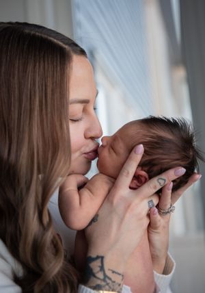 A tender moment captured as a parent with tattoos holds and kisses their newborn baby.