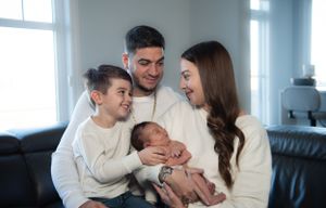 A family sits together on a couch, bonding with their newborn while wearing matching white sweaters.