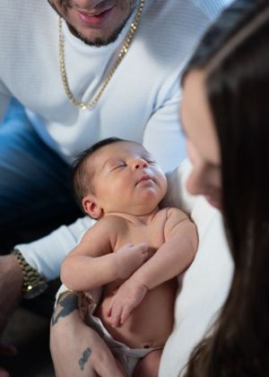A sleeping newborn baby rests on someone wearing a white sweater and gold chain.