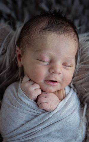 A sleeping newborn wrapped in soft gray fabric smiles contentedly.