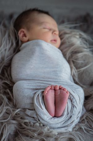 A swaddled newborn sleeping on gray textured fabric with tiny feet peeking out.
