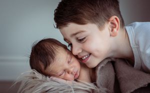 A tender sibling moment as two children rest together on soft bedding.