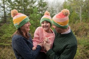 Three people wearing matching colorful winter hats laughing together outdoors.