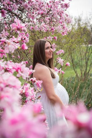 Pink magnolia blossoms frame a spring portrait session with a woman in a white top enjoying the blooming trees.