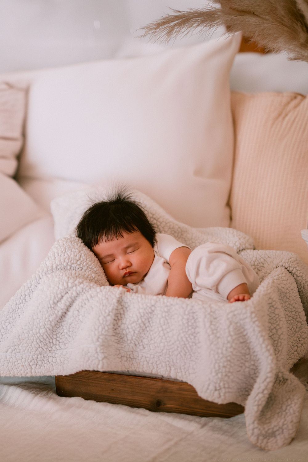 A baby sleeps peacefully under a cozy white sherpa blanket on a comfortable bed.