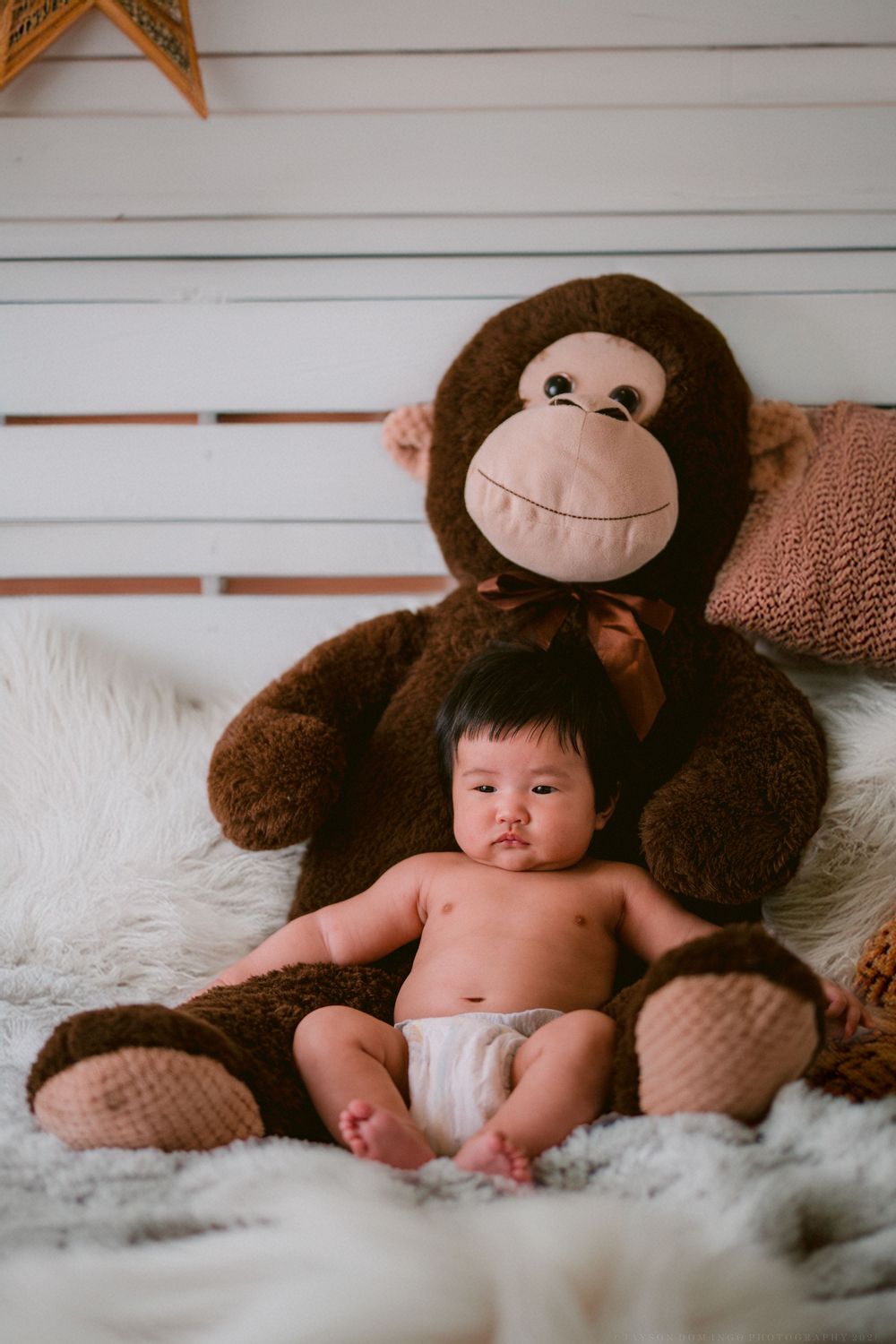 Baby lying on white fur blanket with large brown plush monkey toy in series of connected photos.