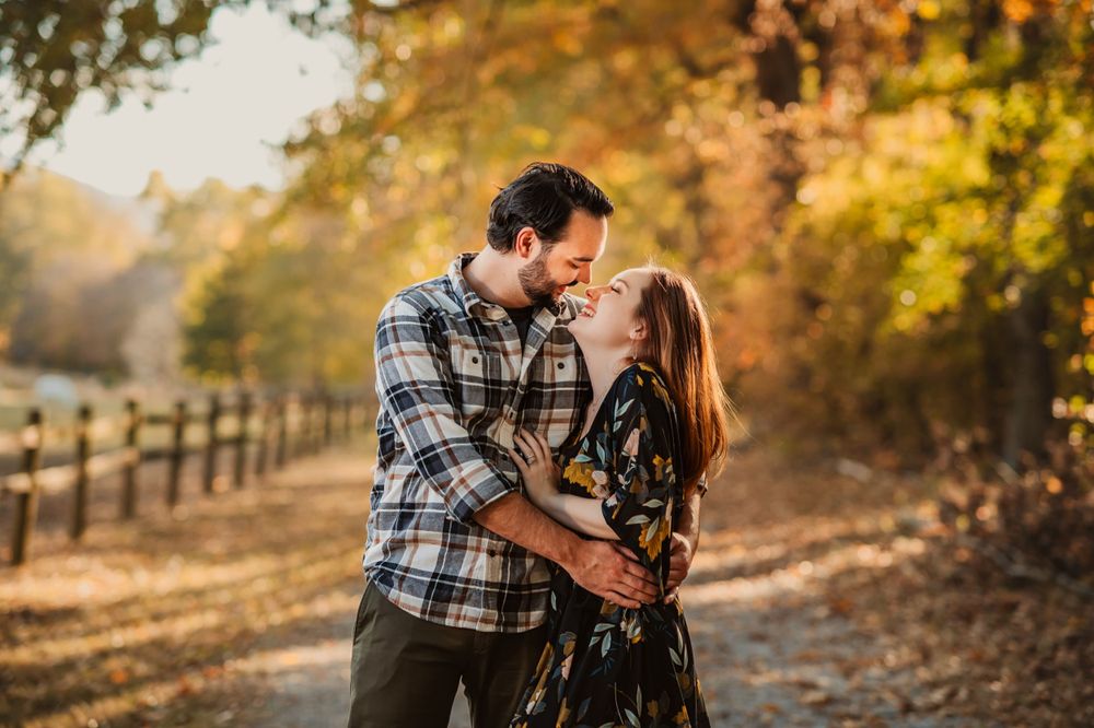 husband and wife laugh at each other while hugging on path through fall trees in Chattanooga