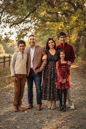A family poses together for a fall portrait on a tree-lined path wearing coordinated autumn colors.