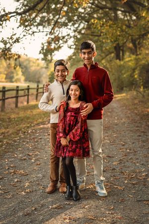 Children playfully interact on a leaf-covered path with wooden fences during a fall photoshoot.