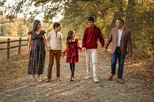 Family walking together on autumn trail with fall foliage in background at sunset.