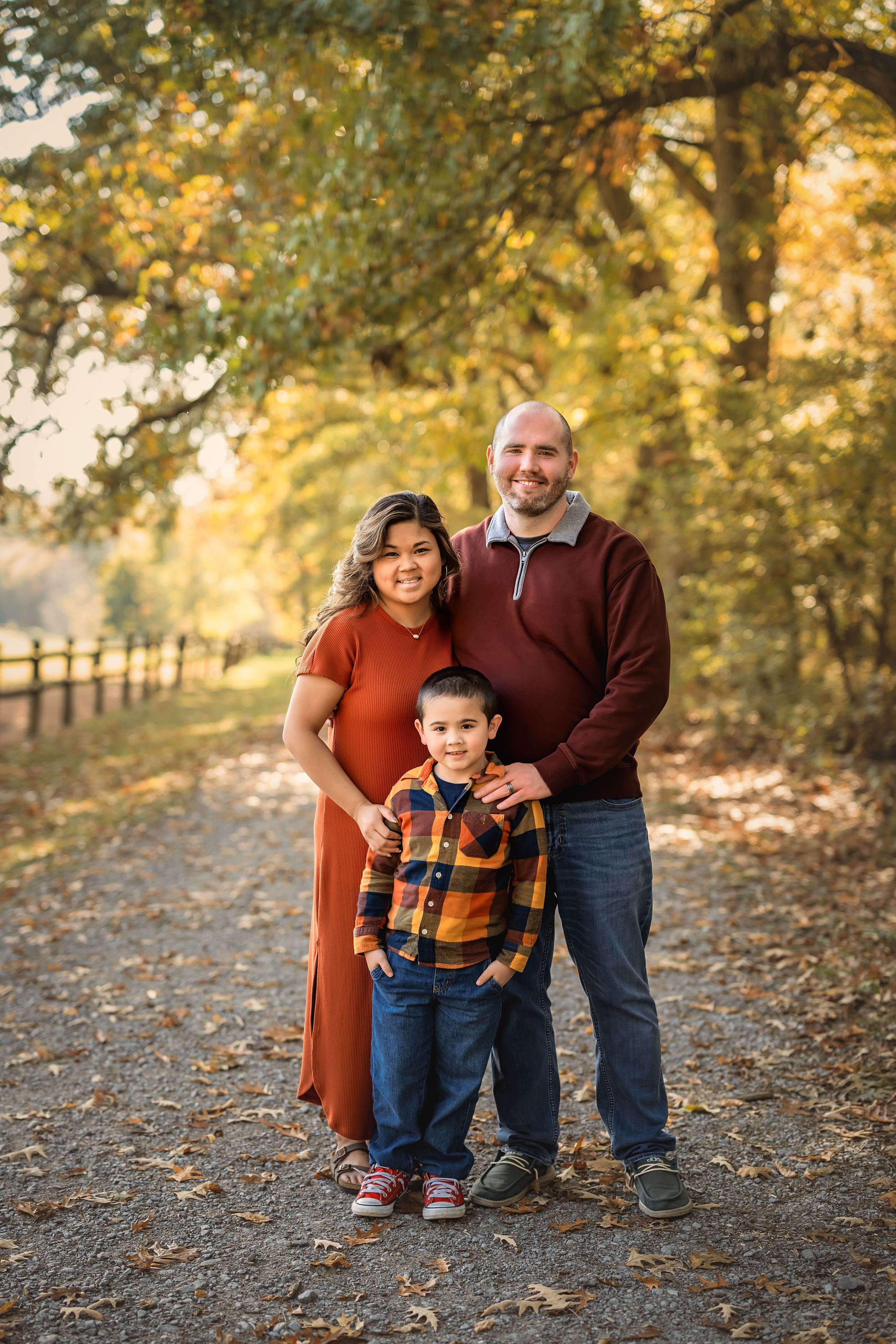 A group portrait in warm autumn colors standing on a leaf-covered path with trees in the background.