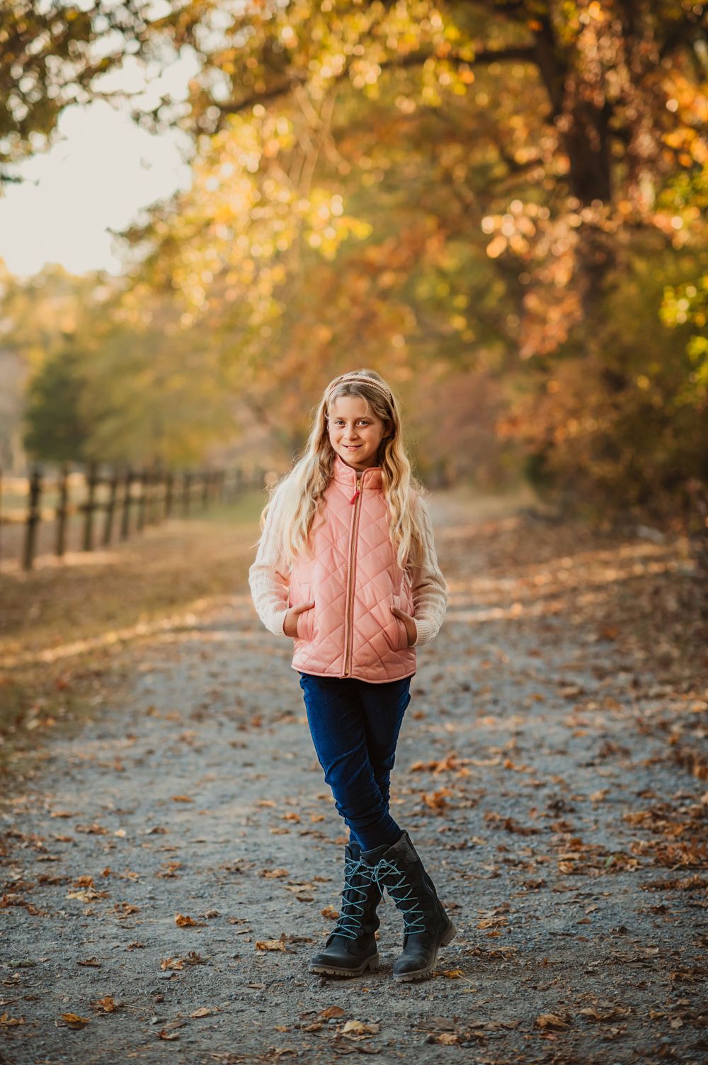 blonde girl in pink puffer crosses legs on fall leaf path in Chattanooga for minis