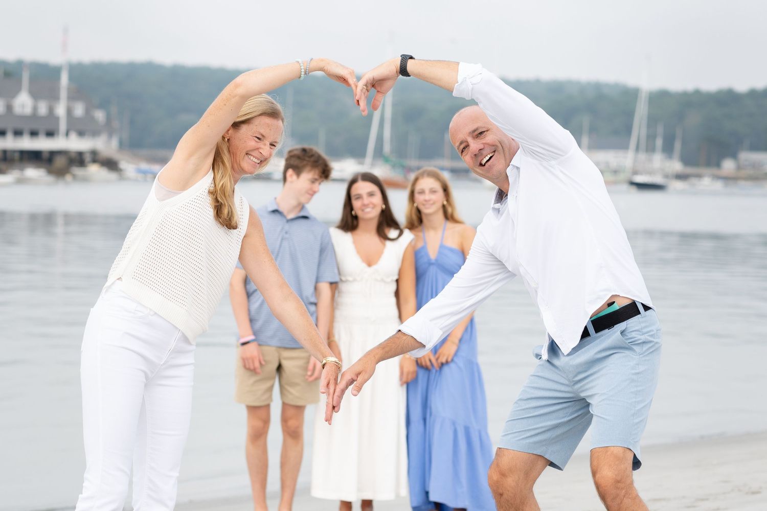 Family members in coordinated white and blue outfits pose playfully by a marina with boats in the background.