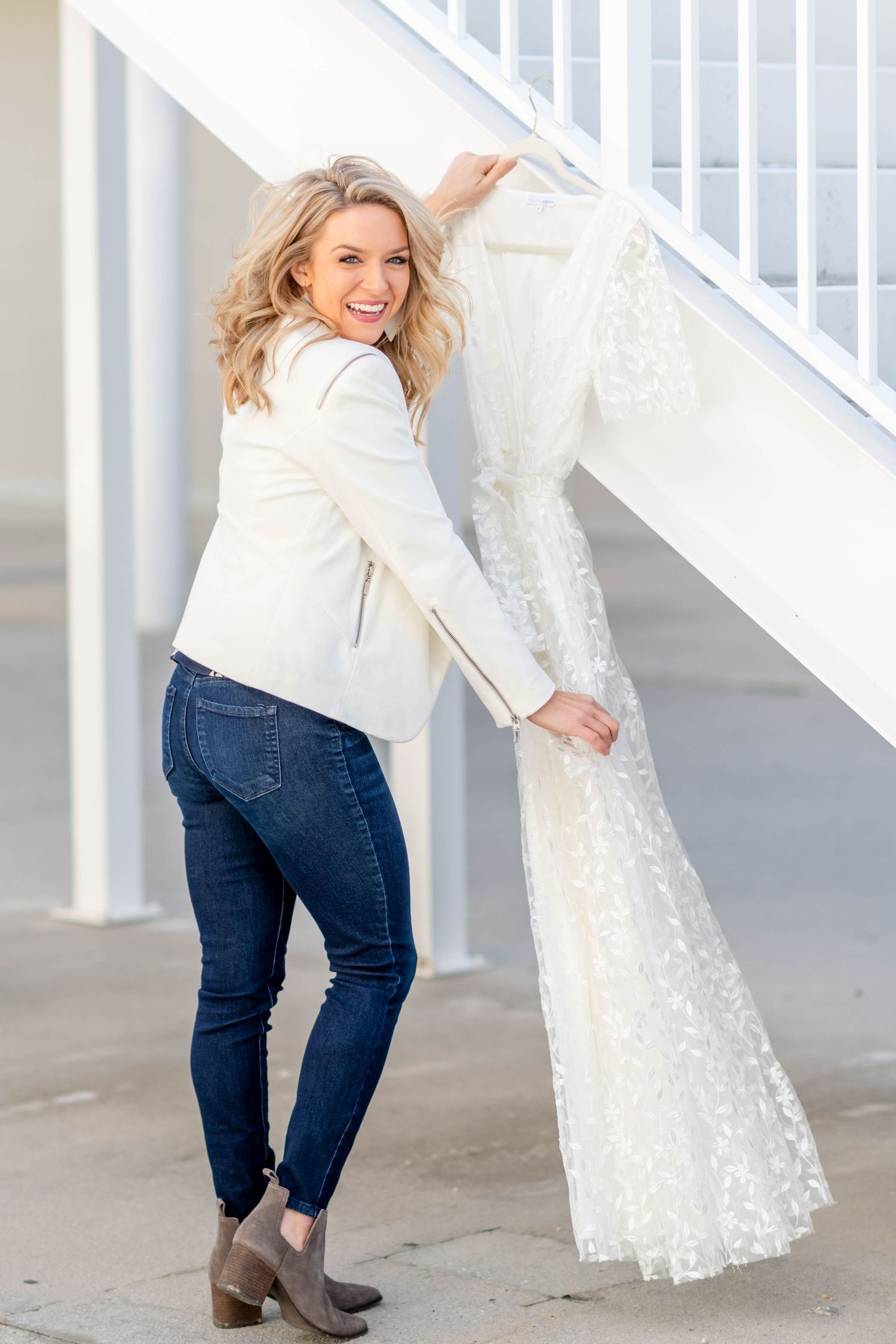 Indiana wedding photographer in white blazer and jeans holds up a lace wedding dress near white staircase. Angela Hartwig photography.