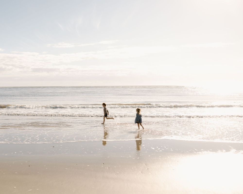 People walking along a misty beach shoreline at sunset with waves rolling onto the sand.