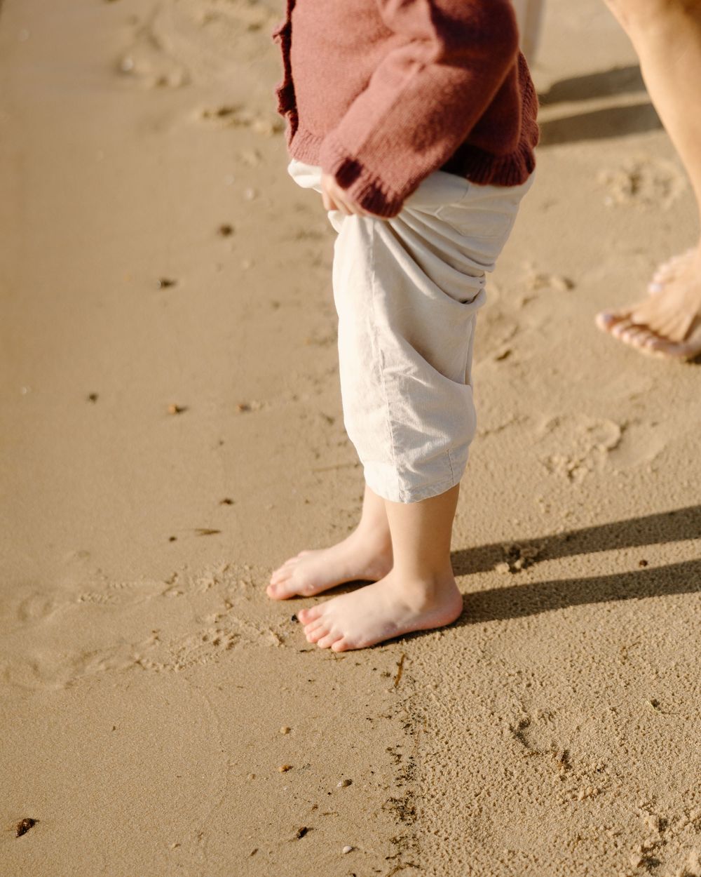 Close-up view of bare feet walking on sandy beach in warm sunlight.