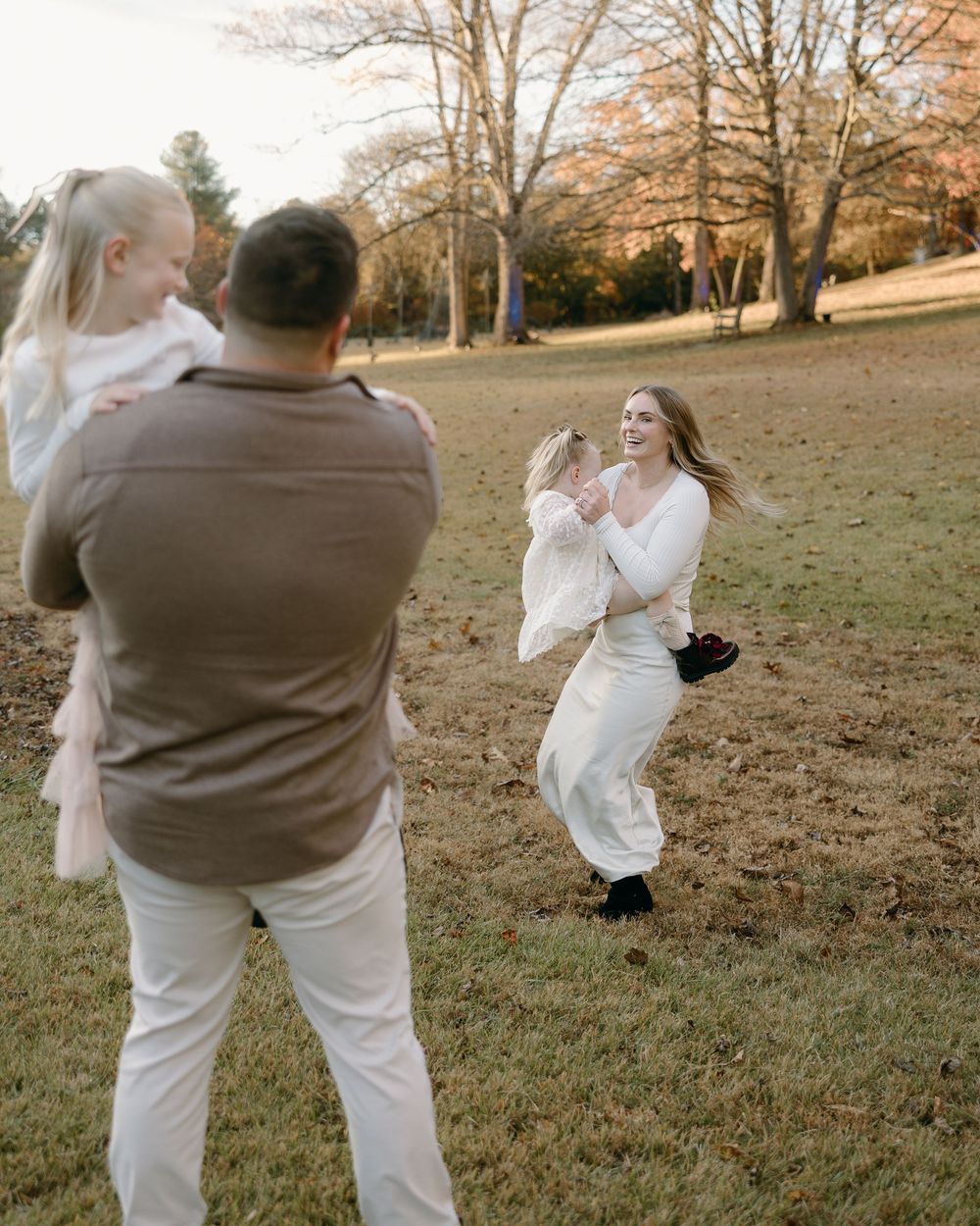 A couple in wedding attire dances and spins playfully in a grassy autumn field during their outdoor photoshoot.