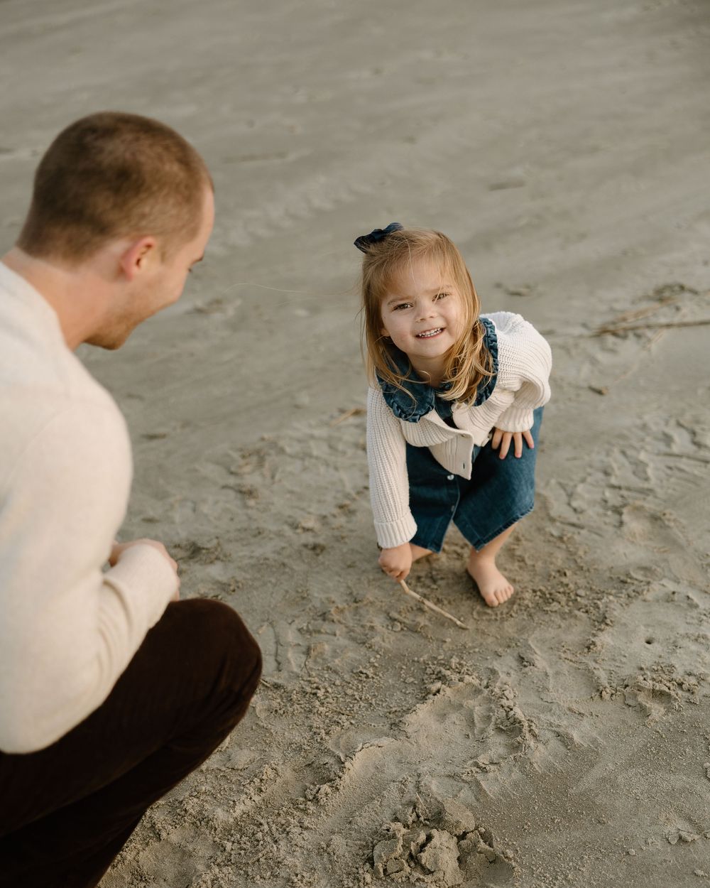 A child draws with chalk on a concrete floor while an adult watches and interacts nearby.
