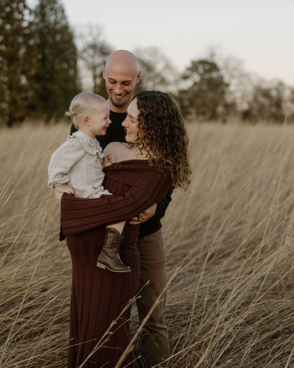 A family shares tender moments together in a golden wheat field at sunset.