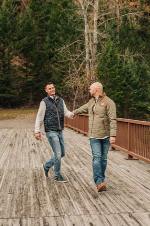 Two people walking and laughing together on a wooden bridge in the mountains.
